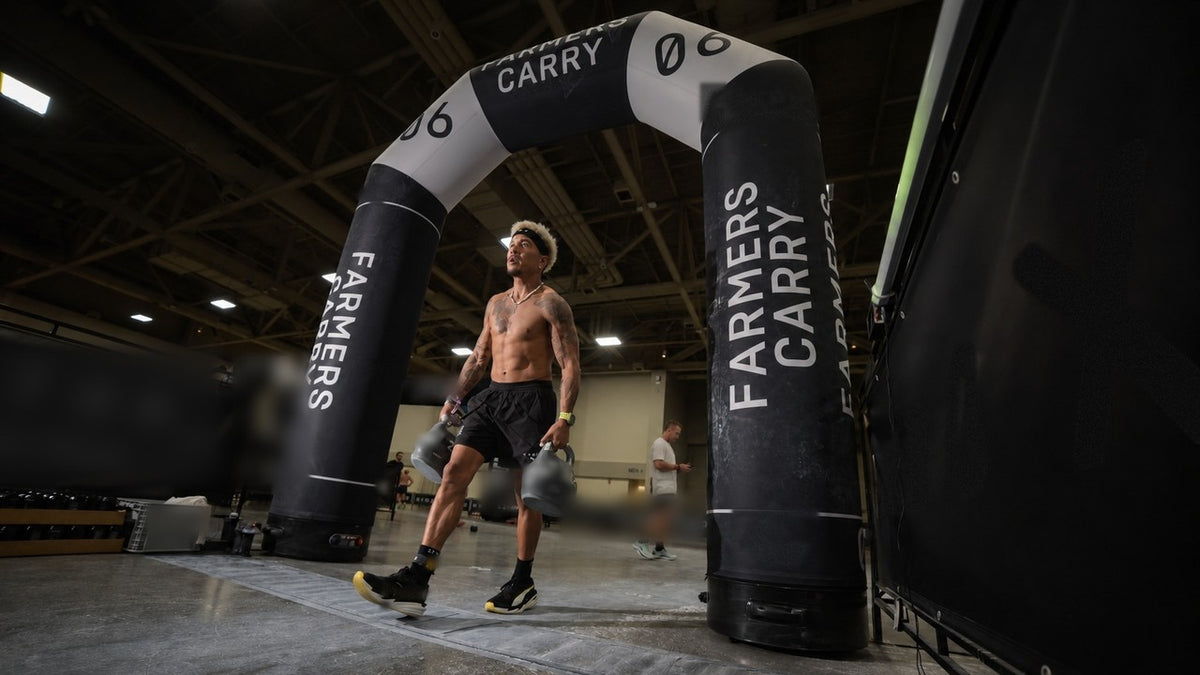 New State founder walking through the farmers carry station with two kettlebells at an indoor hybrid race