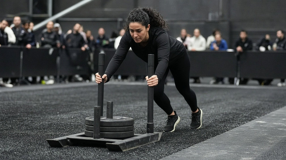 Hybrid race athlete leaning low into a weighted sled push on an indoor race floor