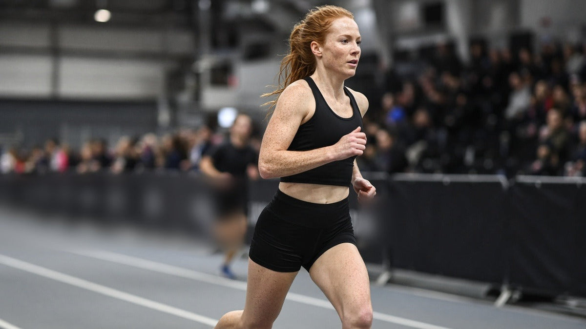 Hybrid race athlete running in plain black race kit on an indoor race floor